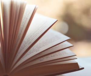 Zbliżenie na otwartą książkę z przewracającymi się kartkami na rozmytym, ciepłym tle, symbolizujące rozwój poprzez czytanie i poszukiwanie inspiracji przywódczych przez liderów HR.