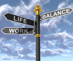 Znak drogowy z trzema czarnymi tabliczkami z napisami „LIFE”, „WORK” i „BALANCE” na tle nieba z chmurami, symbolizujący poszukiwanie równowagi między życiem zawodowym a prywatnym u menedżerów.