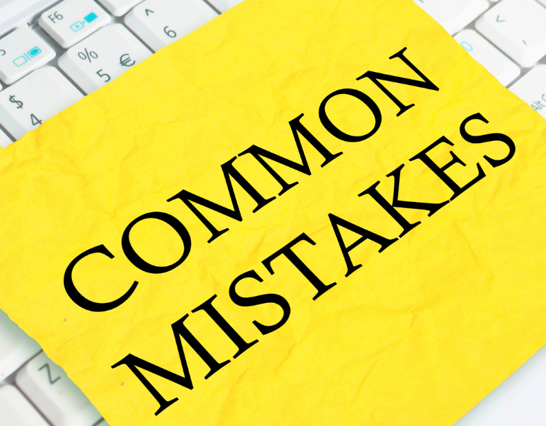 Żółta kartka z napisem „COMMON MISTAKES” leżąca na białej klawiaturze laptopa, symbolizująca typowe błędy popełniane przy współpracy z agencjami pracy tymczasowej.﻿